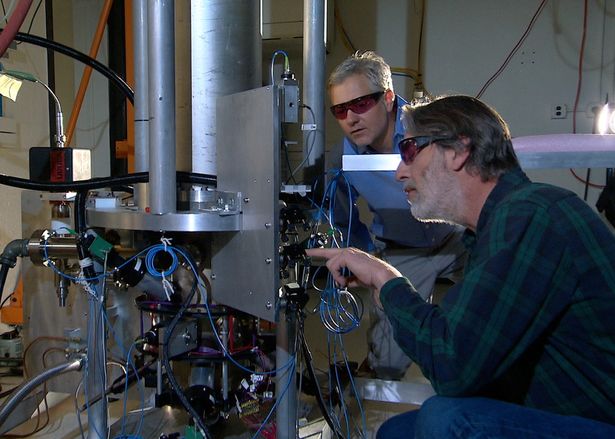 علماء إلى جانب الساعة الذرية NIST-F2 التي تعتمد على نافورة السيزيوم وتُستخدم معيارًا للوقت في الولايات المتحدة (تصوير: NIST / ويكيميديا كومنز، ملكية عامة)
