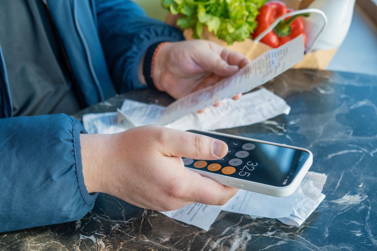 Shopper,Uses,Smartphone,Calculator,While,Reviewing,Grocery,Receipts,Beside,Bag | Shutterstock